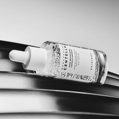 SKIN1004 Tone Brightening Capsule Ampoule 50ml bottle lying diagonally on a dark reflective surface.