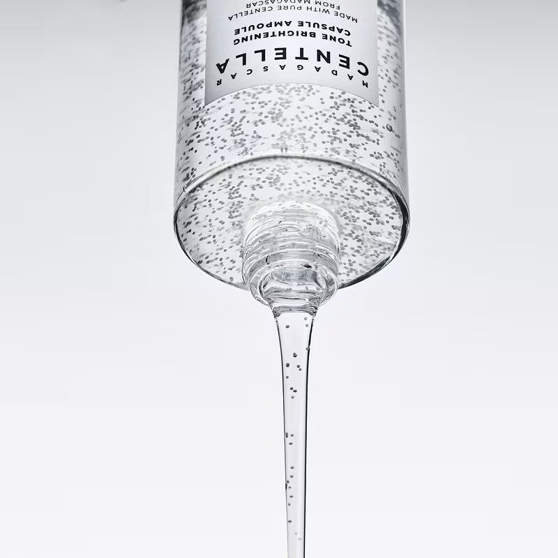 Close-up of capsule-filled SKIN1004 Tone Brightening ampoule pouring from an inverted bottle.