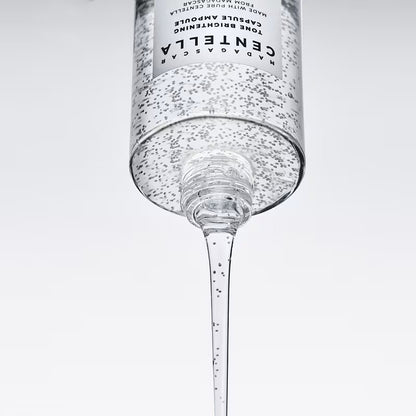 Close-up of capsule-filled SKIN1004 Tone Brightening ampoule pouring from an inverted bottle.