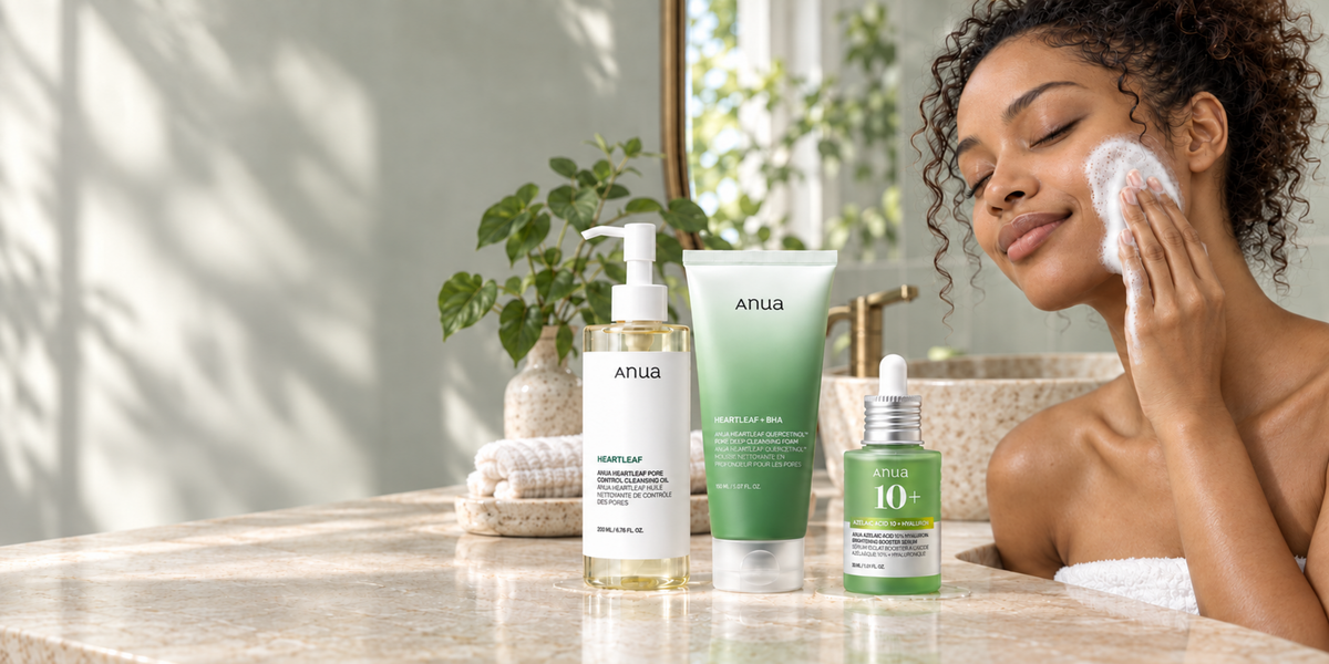 Woman cleansing with foam beside three ANUA skincare products in a softly lit green bathroom.